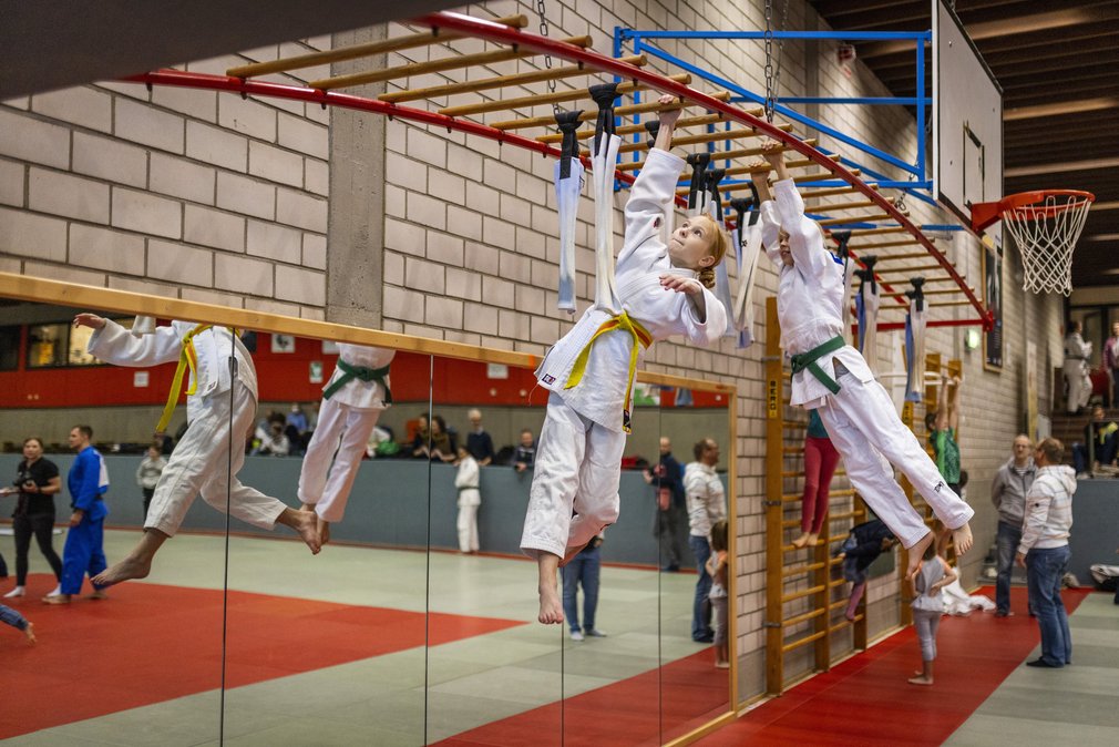 Zwei Maedchen hangeln sich an einer Leiter durch die Turnhalle.