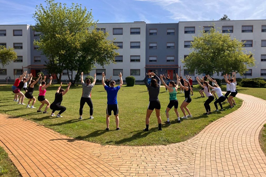 Eine Gruppe von Menschen macht Fitnessuebungen in einem grossen Kreis.