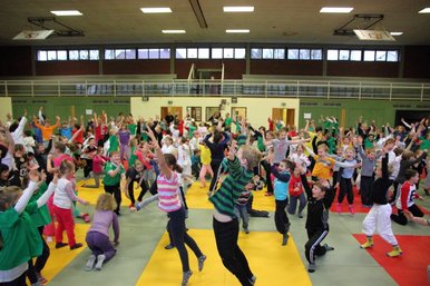 Viele Kinder in einer Sporthalle - huepfend, mit hochgerissenen Armen.