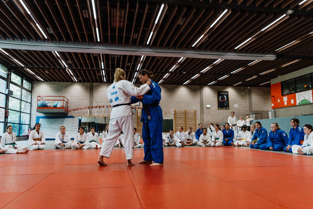 Zwei Maedchen im Ippon Girls Camp bei einem Trainingskampf, waehrend andere im Kreis um sie herum sitzen und zuschauen.
