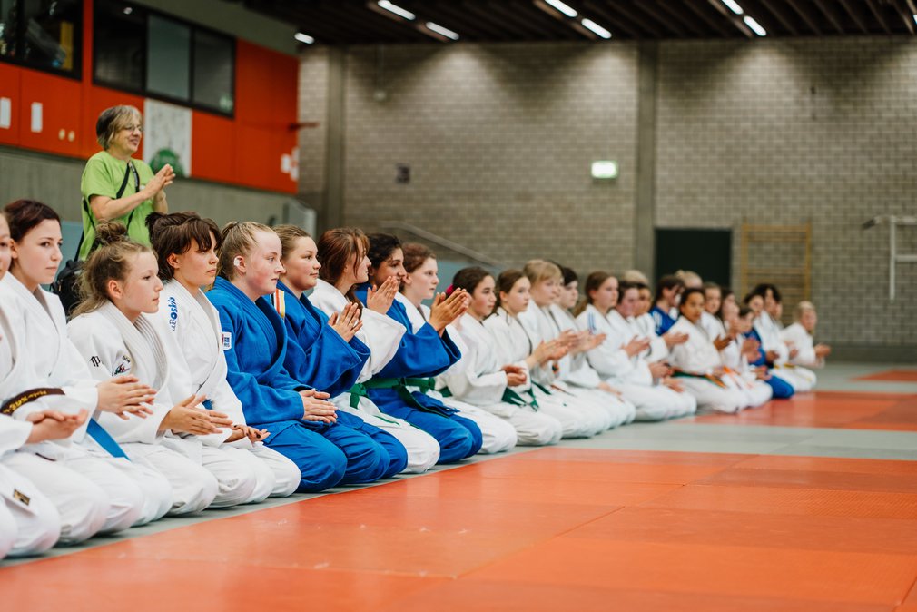 Die Teilnehmerinnnen im Ippon Girls Camp knien in einer Reihe auf dem Boden und feuern andere Judoka an.