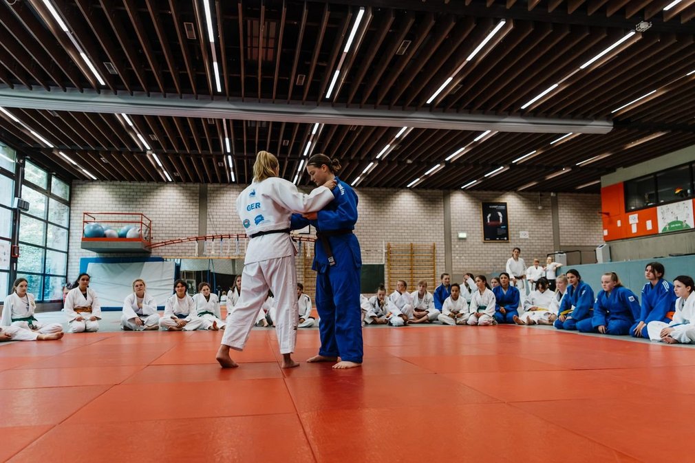 Zwei Maedchen im Ippon Girls Camp bei einem Trainingskampf, waehrend andere im Kreis um sie herum sitzen und zuschauen.