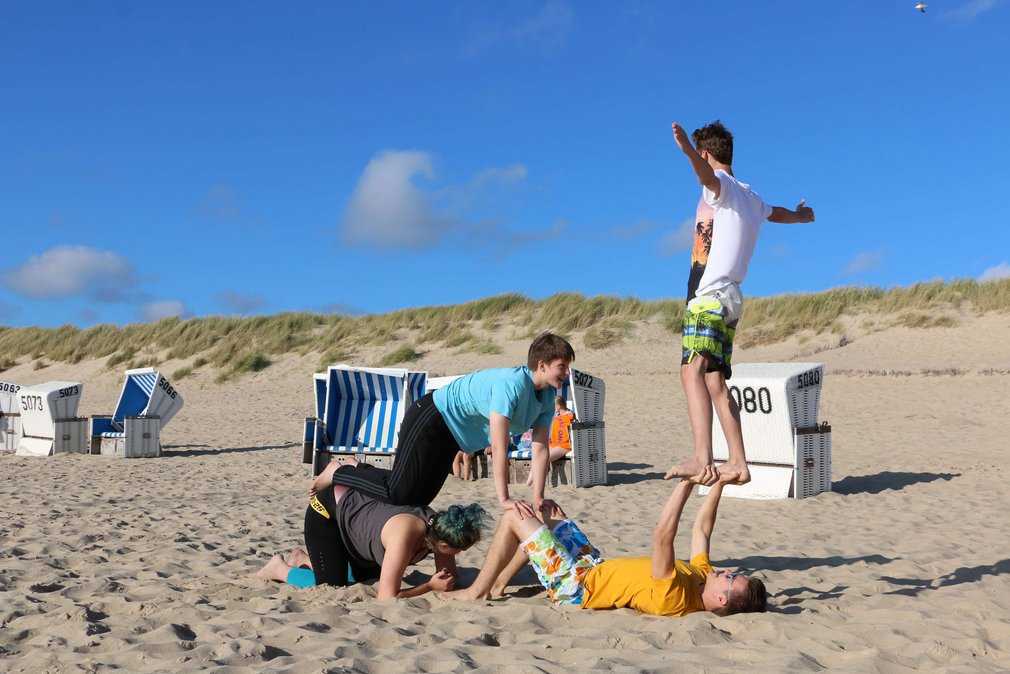 Vier junge Menschen bauen eine Pyramide am Strand.