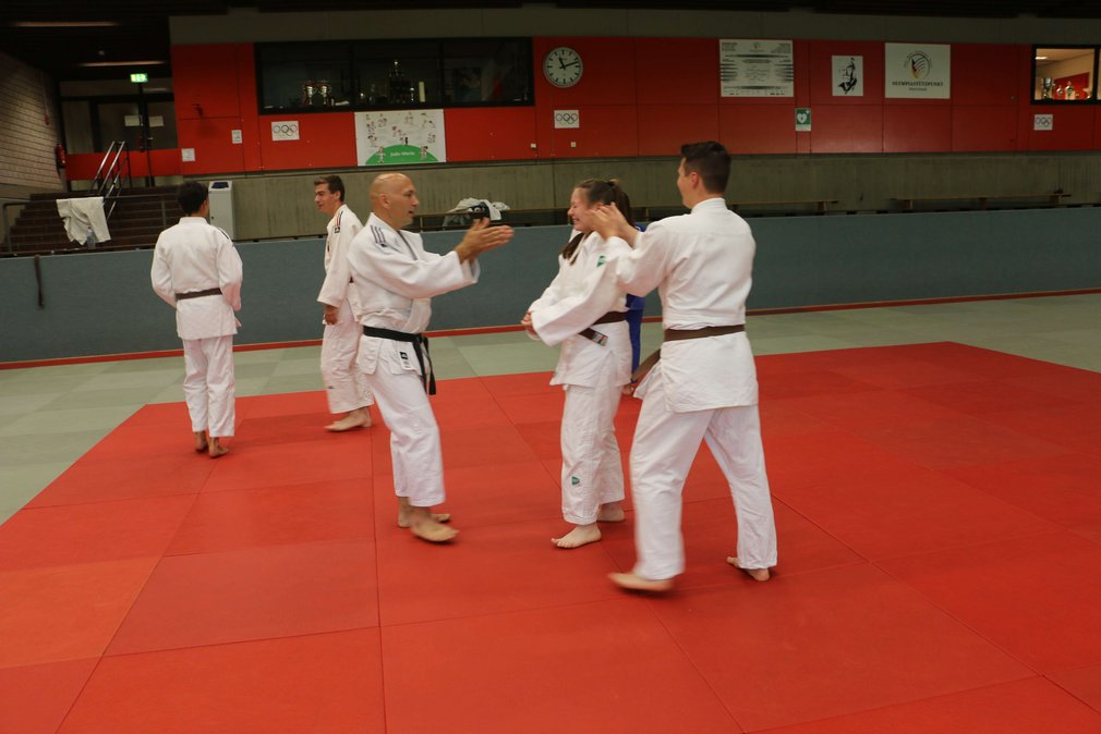 Aeltere und juengere Judoka spielen ein Spiel beim Training in einer Sporthalle.