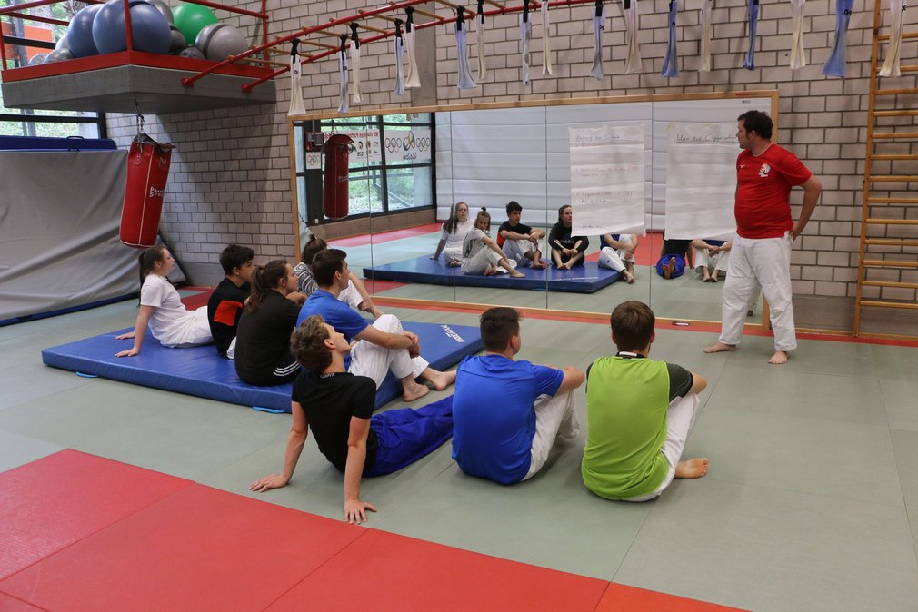 Eine Gruppe Judoka sitzt im Kreis auf dem Boden, um einen Trainer.