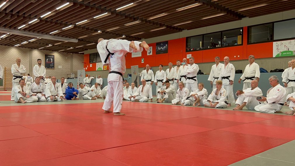 Zwei Judoka praktizieren Kata vor einer Gruppe von weiteren Judoka, die aufmerksam zuschauen.