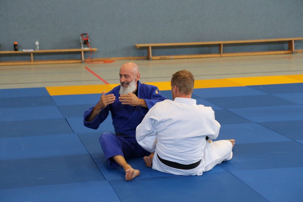 Ein Judotrainer erklaert der Gruppe etwas an einem anderen Teilnehmer.