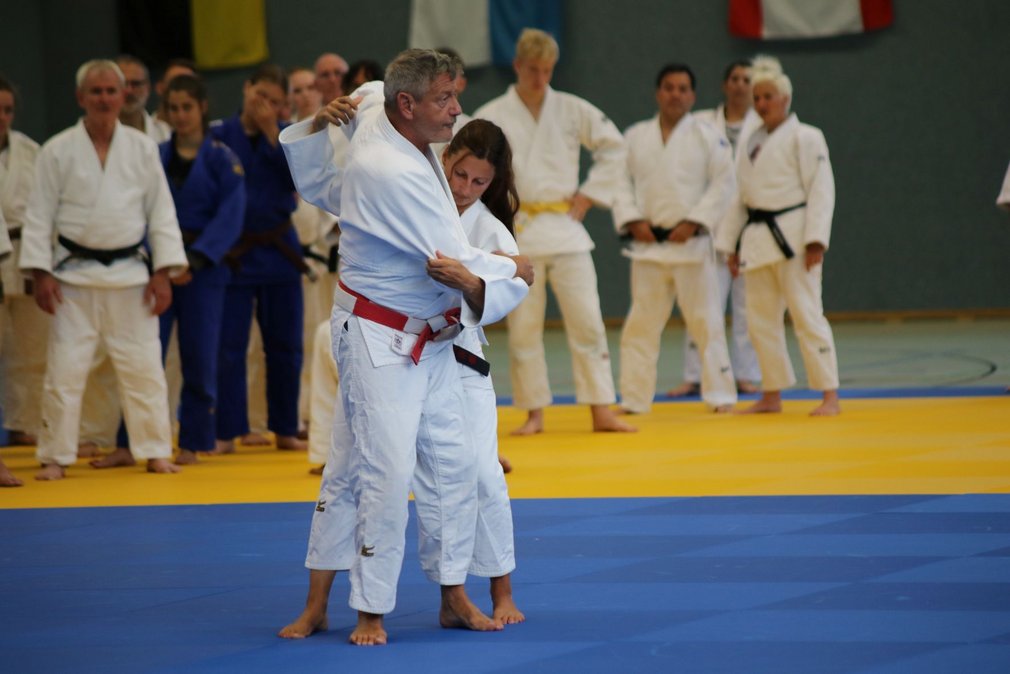 Zwei Judoka beim Training, waehrend die anderen Teilnehmenden um sie herum stehen und zuschauen.