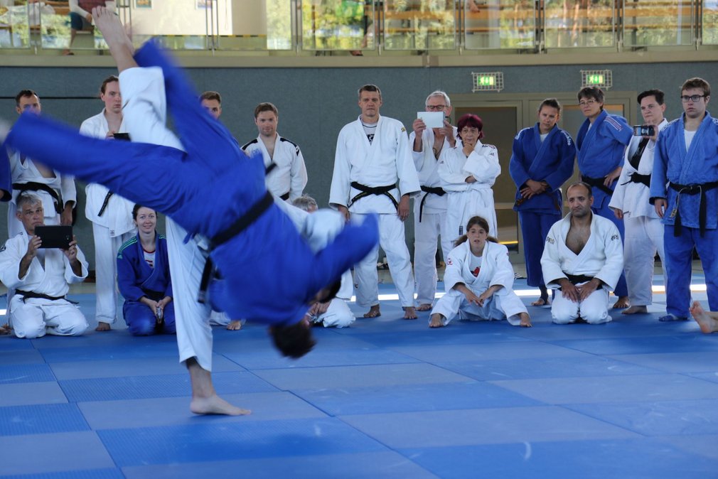 Zwei Judoka bei einem Trainingskampf, waehrend die anderen Teilnehmenden um sie herum stehen und zuschauen.