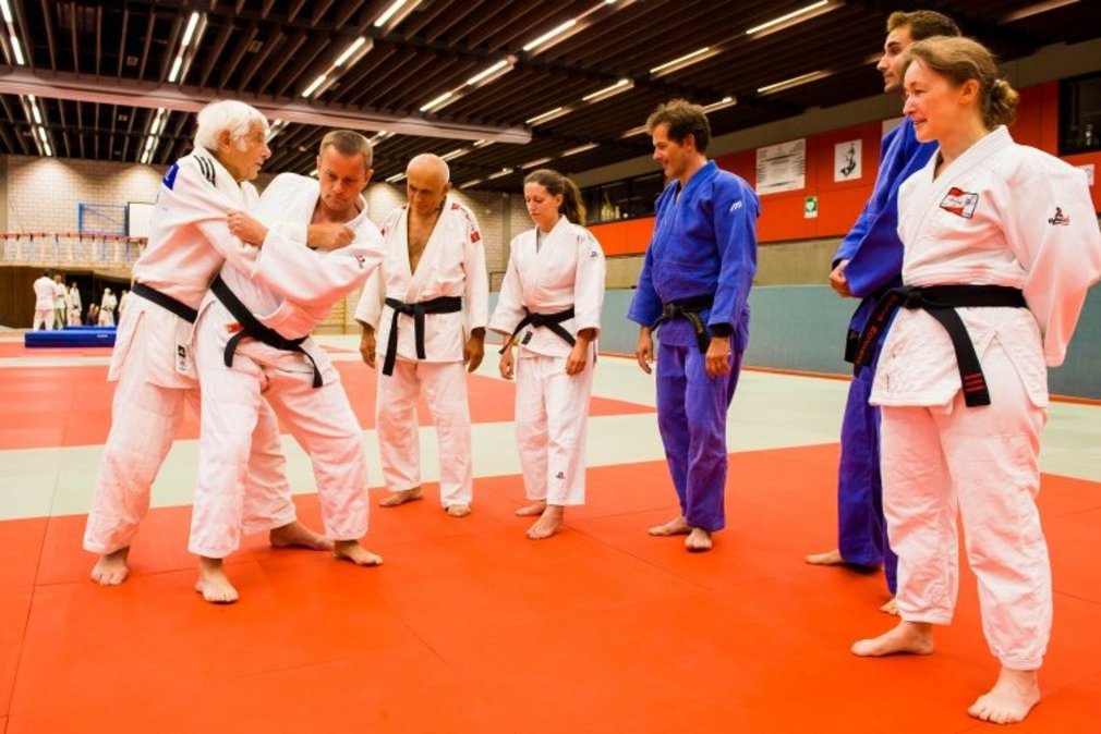Zwei Judoka im Training, waehrend weitere Judoka um sie herum stehen und ihnen zuschauen