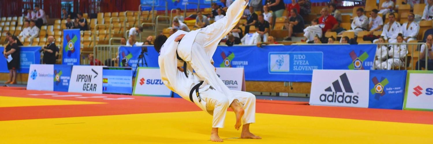 Zwei Judokas bei einem Wettkampf, mit einigen Zuschauern im Hintergrund.