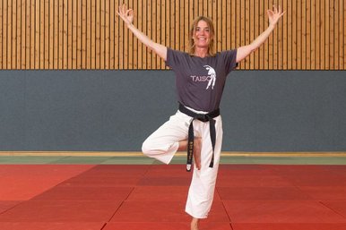 Eine Judoka, die eine Gleichgewichtsuebung durchfuehrt und in die Kamera laechelt