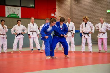 Zwei Judoka trainieren miteinander, waehrend um sie herum weitere Judoka in einem Kreis stehen