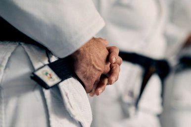 Nahaufnahme von den Haenden eines Judoka, die gefaltet auf dem schwarzen Guertel liegen