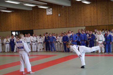 Zwei Judoka zeigen etwas und werden dabei von vielen umstehenden Judoka beobachtet.