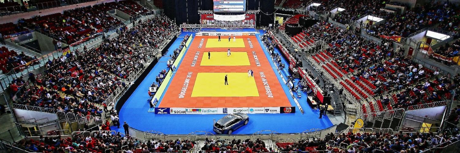 Eine Wettkampfhalle mit vielen Zuschauern und drei Wettkampfflaechen.