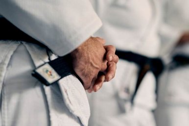 Detailaufnahme von den Haenden eines Judoka, die ueber seinem schwarzen Guertel gefaltet sind 