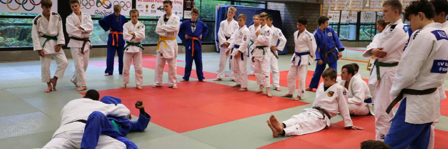 Zwei jugendliche Judoka im Trainingskampf, die von umstehenden Judoka beobachtet werden.