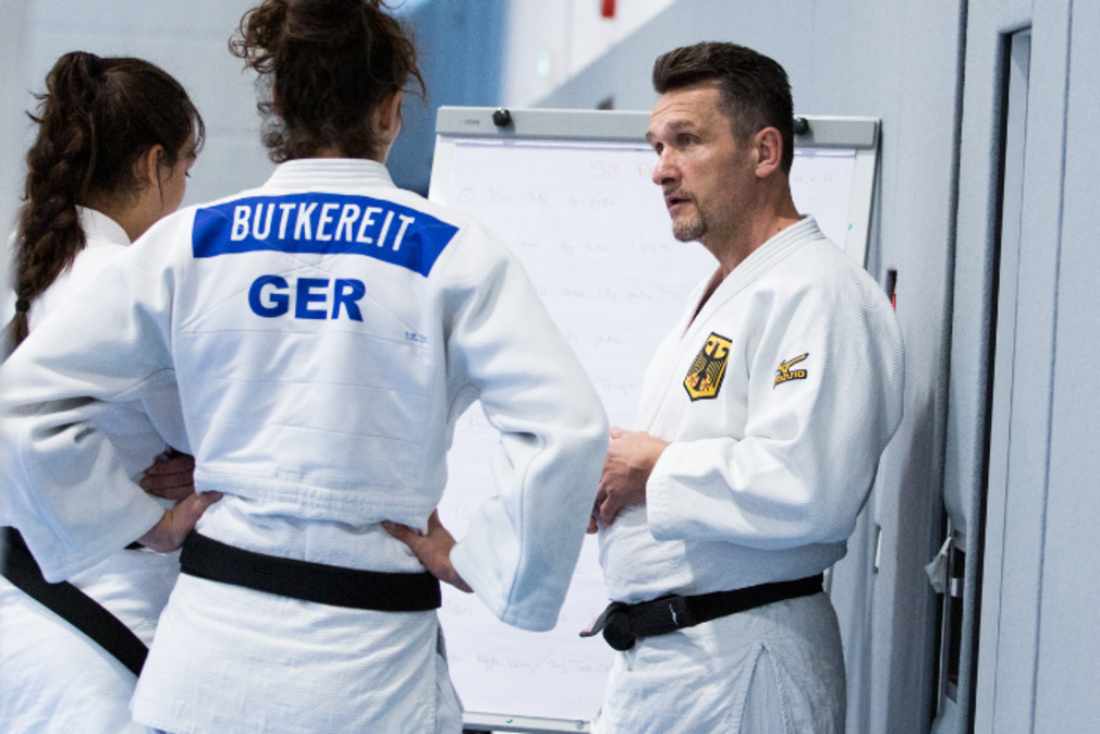 Ein Judotrainer, der zwei Judoka etwas erklaert.