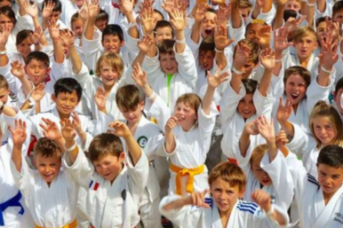 Viele Kinder in Judoanzuegen winken in die Kamera
